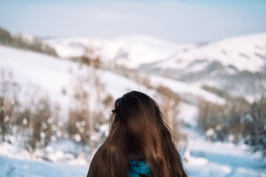 Girl in front of snowy mountains and forest.
