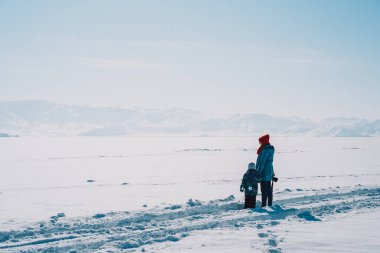Mom and son in winter clothes standing on a snowy field.