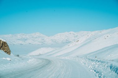 Snowy road among fields and mountains.