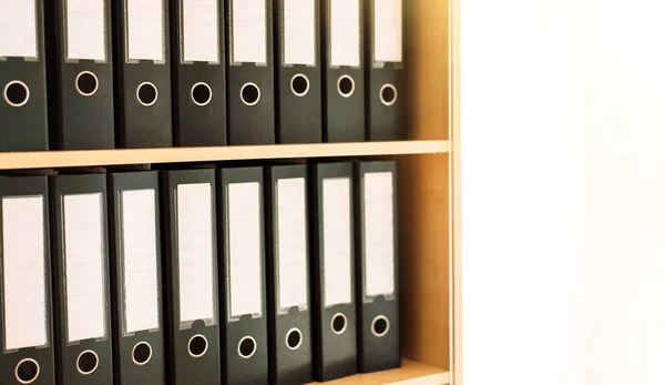 Black office folders standing on cabinet shelves.