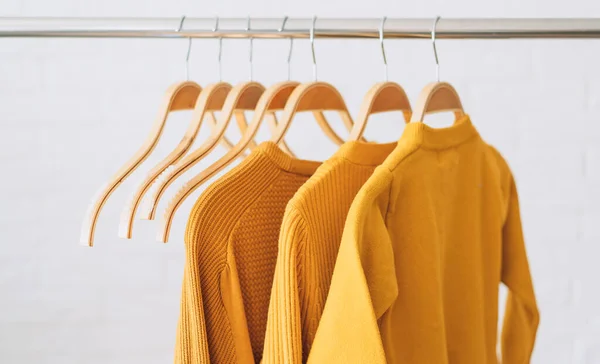 Yellow sweatshirts on wooden hangers hang on an iron bar rale.