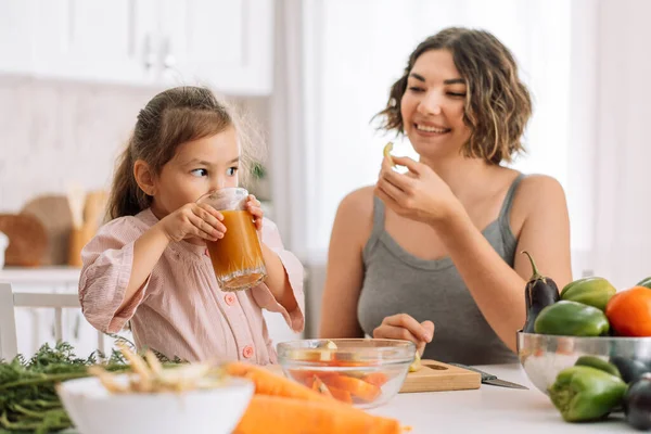 Mom and daughter eat chopped vegetables and drink freshly squeezed juice.