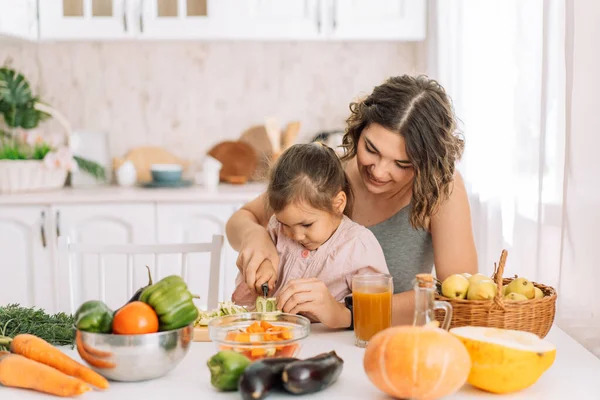 Mom and daughter cut vegetables together at the table.