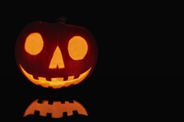 Karanlıkta yanan bir Jack O 'Lantern' a yaklaş ve önündeki siyah yüzeyi yansıt..