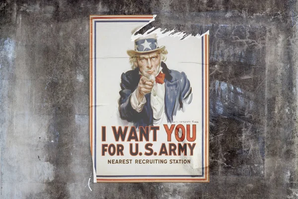 Full-frame weathered concrete wall with a torn poster in the middle depicting Uncle Sam with 