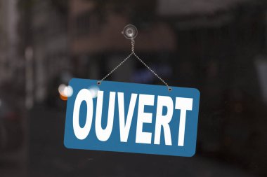 Bir dükkanın vitrinindeki mavi tabelaya yakın çekimde Fransızcada mesajı gösterir - İngilizce 'de Ouvert - Aç -.
