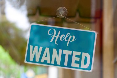 Close-up on a blue sign in the window of a shop displaying the message - Help wanted -.