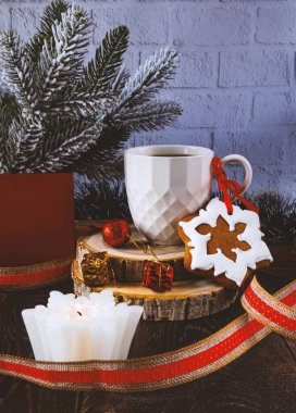 Gingerbread, a cup of coffee and a candle. Festive Christmas and New Year composition with a gift ribbon. Wooden background and branches of the Christmas tree. Side view.