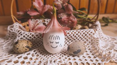 Gülümseyen bir Paskalya yumurtası. Paskalya sepetinin etrafında bıldırcın yumurtaları ve pembe alstroemeryalar var. Paskalya havası.