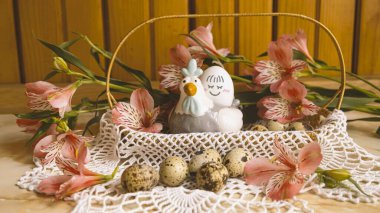 Easter basket with quail eggs and flowers. Decorative chicken with egg with a smile. Pink alstroemerias around. clipart