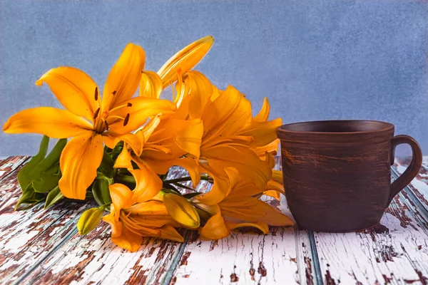 A bouquet of yellow lilies on a vintage blue background. Vintage brown cup of coffee on the table. Summer still life