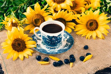 A bouquet of sunflowers in a rustic style. A white and blue cup, blueberries on the table. Summer still life.Top view