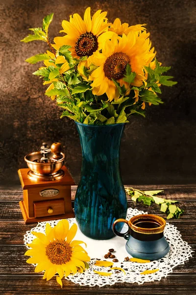 A bouquet of sunflowers in a blue vase on a dark background in a rustic style. Blue cup of coffee and vintage coffee grinder on the table. Side view