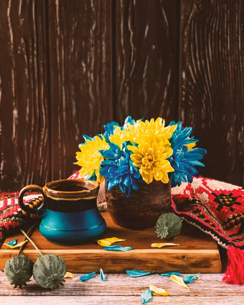 A blue-yellow bouquet of chrysanthemums in a vintage cup. Patriotic composition for the Independence Day of Ukraine with a ripe poppy, a blue cup of coffee and an embroidered towel.