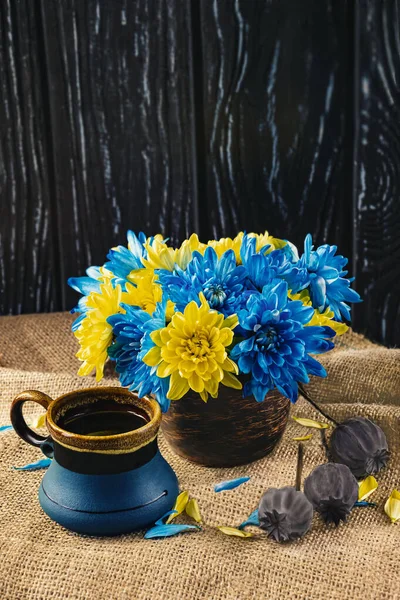 Blue and yellow chrysanthemum flowers and a blue cup of coffee and a ripe poppy. Patriotic composition for the Independence Day of Ukraine with the colors of the flag. Side view.