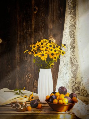 Erik, sarı erik, balkabağı ve Rudbeckia çiçekleriyle dolu beyaz bir vazoda sonbahar. Penceresinde güneş ışığı olan kompozisyon. Yan görünüm.