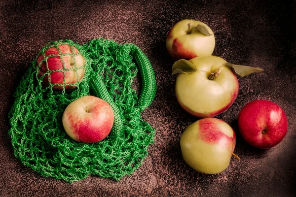 Ripe green and red apples in a green eco-bag on a dark background. Fresh harvest of apples on the table on a dark background.