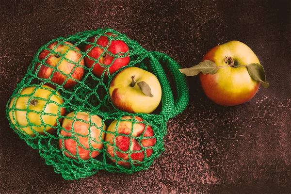 Ripe green and red apples in a green eco-bag on a dark background. Fresh harvest of apples on the table on a dark background.