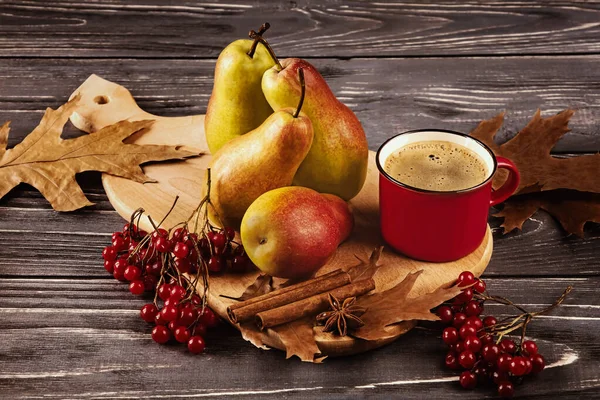 Yellow-red ripe pears and a red cup of coffee on a wooden board on a dark background. Autumn composition of fruits with autumn leaves, viburnum, with spices, cinnamon and anise. Side view