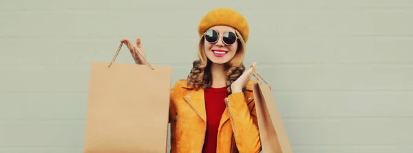 秋の肖像画の美しいです幸せな笑顔若い女性でショッピングバッグを身に着けている黄色のジャケット ベレー帽上灰色の背景 — ストック写真
