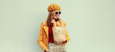 Güzel gülümseyen genç bir kadının portresi. Elinde alışveriş poşeti ve gri arka planda uzun beyaz ekmek ekmeği var.