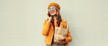 Akıllı telefondan arayan mutlu bir kadının portresi. Elinde gri arka planda uzun beyaz ekmek ekmeği olan bir alışveriş poşeti var.