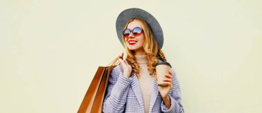 Güzel, mutlu, gülümseyen genç bir kadının sonbahar portresi. Alışveriş poşetleri ve kahve fincanı olan, beyaz arka planda şapkası olan.