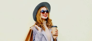 Güzel, mutlu, gülümseyen genç bir kadının sonbahar portresi. Alışveriş poşetleri ve kahve fincanı olan, beyaz arka planda şapkası olan.