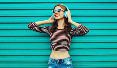 Renkli mavi bir arka planda müzik dinleyen, kulaklıklı mutlu, genç bir kadının portresi.