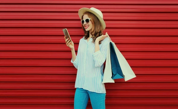 ショッピングバッグやスマートフォンを身に着けている幸せな笑顔の女性の肖像画カラフルな赤の背景にラウンド帽子とシャツ — ストック写真