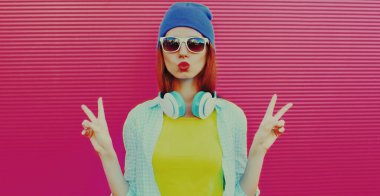 Modern genç kadının renkli yaz portresi pembe arka planda kulaklıkla müzik dinliyor.