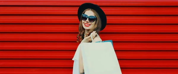 赤い背景に黒い丸帽子を身に着けているショッピングバッグと美しい笑顔の女性の肖像 — ストック写真