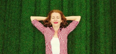 Mutlu gülümseyen genç bir kadının portresi parkta çimlerin üzerinde uzanmış.