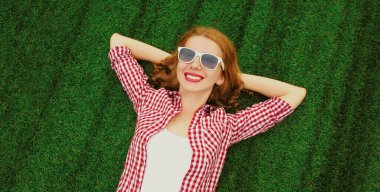 Mutlu gülümseyen genç bir kadının portresi parkta çimlerin üzerinde uzanmış.