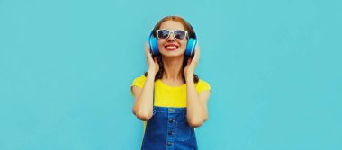 Renkli mavi bir arka planda müzik dinleyen, kulaklıklı mutlu, genç bir kadının portresi.