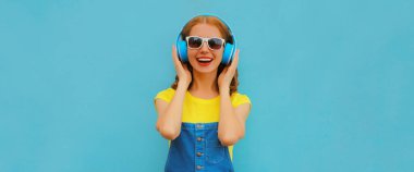 Renkli mavi bir arka planda müzik dinleyen, kulaklıklı mutlu, genç bir kadının portresi.