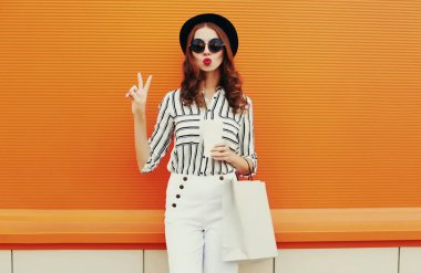 Beyaz çizgili gömlek giyen, turuncu arka planda siyah şapkalı güzel bir genç kadının portresi.