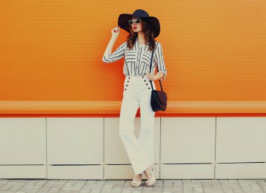 Beyaz çizgili gömlek giyen güzel bir genç kadın portresi, turuncu arka planda siyah yuvarlak şapka.