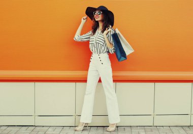 Beyaz çizgili gömlek giyen, turuncu arka planda siyah şapkalı güzel bir genç kadının portresi.