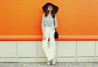 Beyaz çizgili gömlek giyen güzel bir genç kadın portresi, turuncu arka planda siyah yuvarlak şapka.