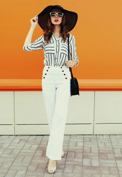 Beyaz çizgili gömlek giyen güzel bir genç kadın portresi, turuncu arka planda siyah yuvarlak şapka.