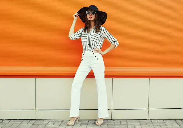 Beyaz çizgili gömlek giyen, turuncu arka planda siyah şapkalı güzel bir genç kadın portresi.