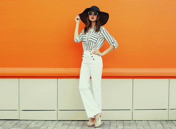 Beyaz çizgili gömlek giyen, turuncu arka planda siyah şapkalı güzel bir genç kadın portresi.