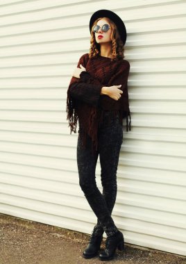 Kahverengi örgü panço giyen güzel bir genç kadın portresi, beyaz arka planda siyah yuvarlak şapka.