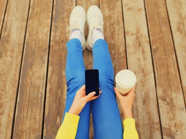 Boş ekran akıllı telefonu ve bir fincan kahveyle ahşap zeminde oturan kadın ellerini kapat.