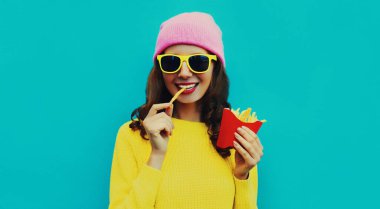 Modaya uygun gülümseyen genç bir kadının portresi hamburger ve patates kızartması ile mavi renkli arka planda.