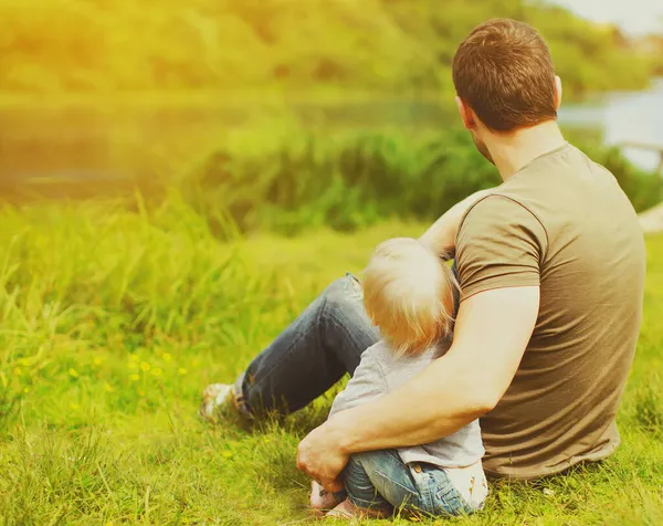 父と息子のバックビュー一緒に離れて川の近くに緑の草の夏に見て座って休んで — ストック写真