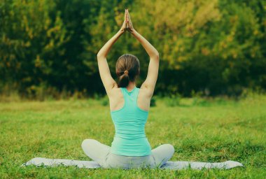Yaz parkında çimlerin üzerinde yoga egzersizleri yapan genç bir kadın.