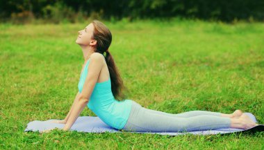 Spor salonundaki kadın yoga egzersizleri yapıyor yaz parkında çimlerin üzerinde esniyor.