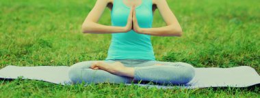 Yaz parkında çimlerin üzerinde yoga egzersizleri yapan genç bir kadın.